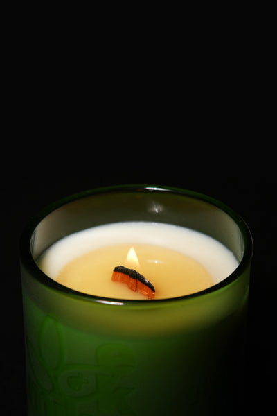 green candle that is burning containing coco butter wax. It has a wooden wick and EkoMiko logo.
